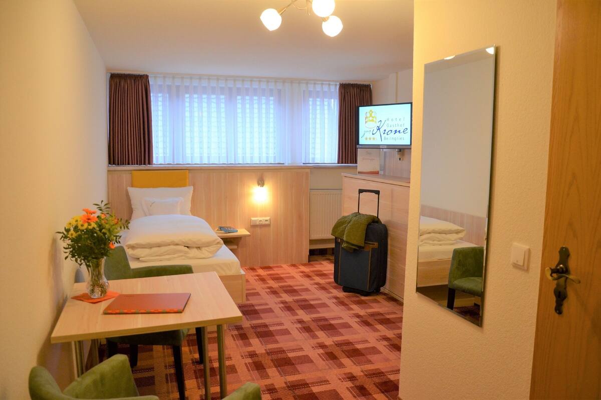 Habitación de hotel con cama, escritorio, silla, maleta y televisor mostrando el nombre del hotel.