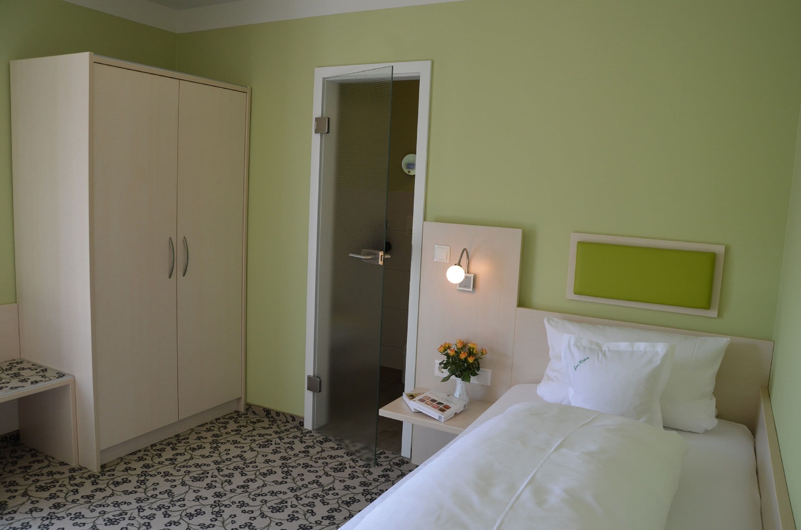 A hotel room with a bed, a nightstand, a wardrobe, and a bathroom door.