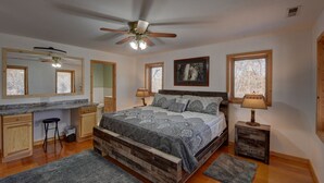 A bedroom with a wooden bed, a ceiling fan, a large window, and a desk area. - Secluded home on 24 acres (Hayesville)