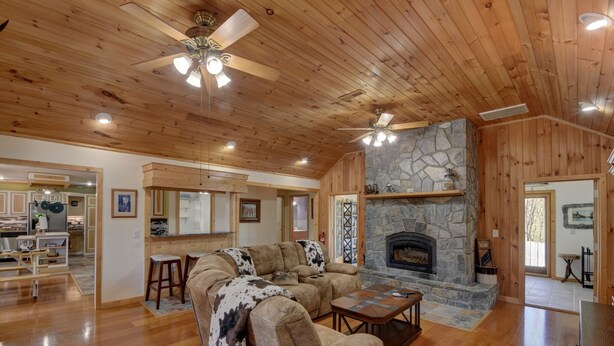 A spacious living room with wooden floors, a stone fireplace, and a large sectional sofa. - Secluded home on 24 acres (Hayesville)