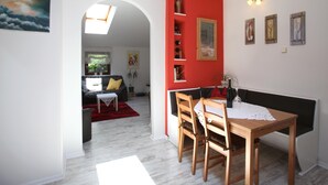 Ein Essbereich mit Holztisch und Stühlen, einer roten Akzentwand und Blick in das Wohnzimmer.