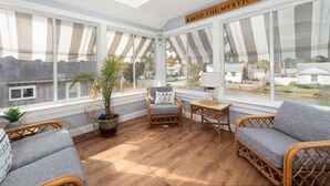 A sunroom with large windows, wicker furniture, and a "Into the Mystic" sign.