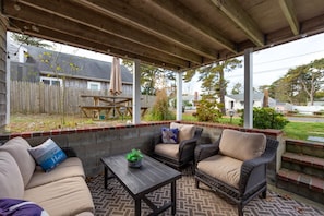 A covered patio area with wicker furniture, a table, and a view of a residential neighborhood.
