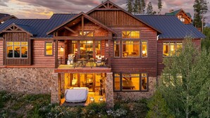 Une grande cabane en rondins à plusieurs étages, dotée de fondations en pierre, de nombreuses fenêtres et d’un balcon.
