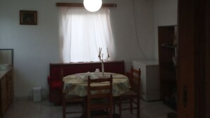 Un comedor con una mesa y sillas, una lámpara colgante, una ventana con cortinas y un radiador en la pared.