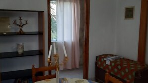 Una habitación con una mesa redonda cubierta por un mantel estampado, un candelabro, una silla, una cama con un edredón estampado, una estantería con objetos decorativos y una ventana con cortinas.