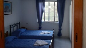 Una habitación con dos camas, una ventana con cortinas, techo de madera y un cuadro colgado en la pared.