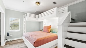 Quarto com uma cama beliche, uma mesinha de cabeceira, janela com persianas e luminária no teto.