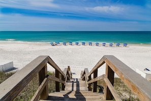Una passerella di legno che conduce a una spiaggia con ombrelloni e lettini blu.