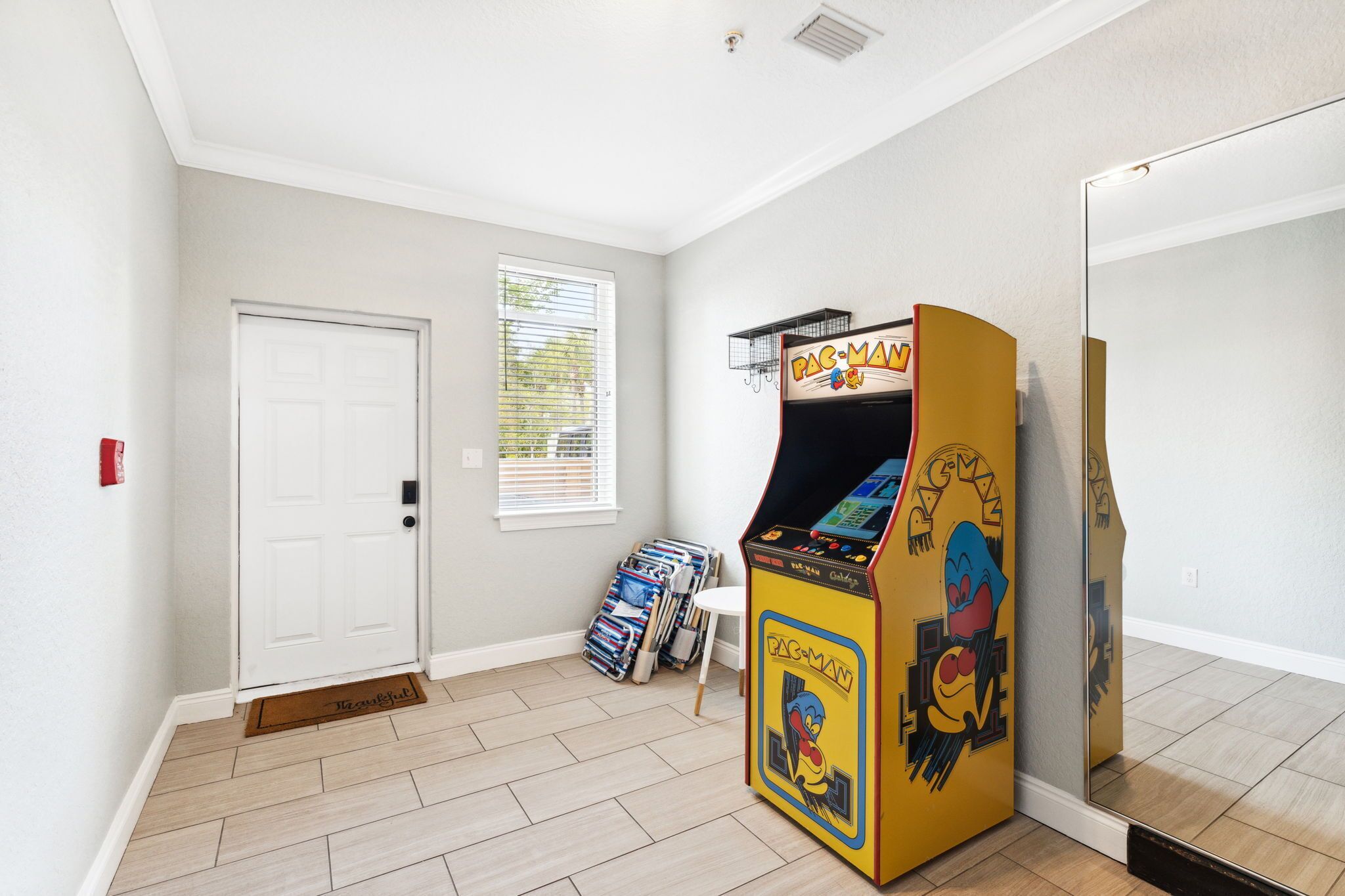 Una habitación con una máquina arcade de Pac-Man, una puerta blanca y un ventanal con persianas.