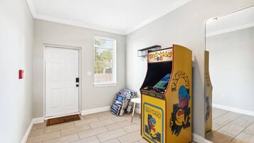Una habitación con una máquina arcade de Pac-Man, una puerta blanca y un ventanal con persianas.