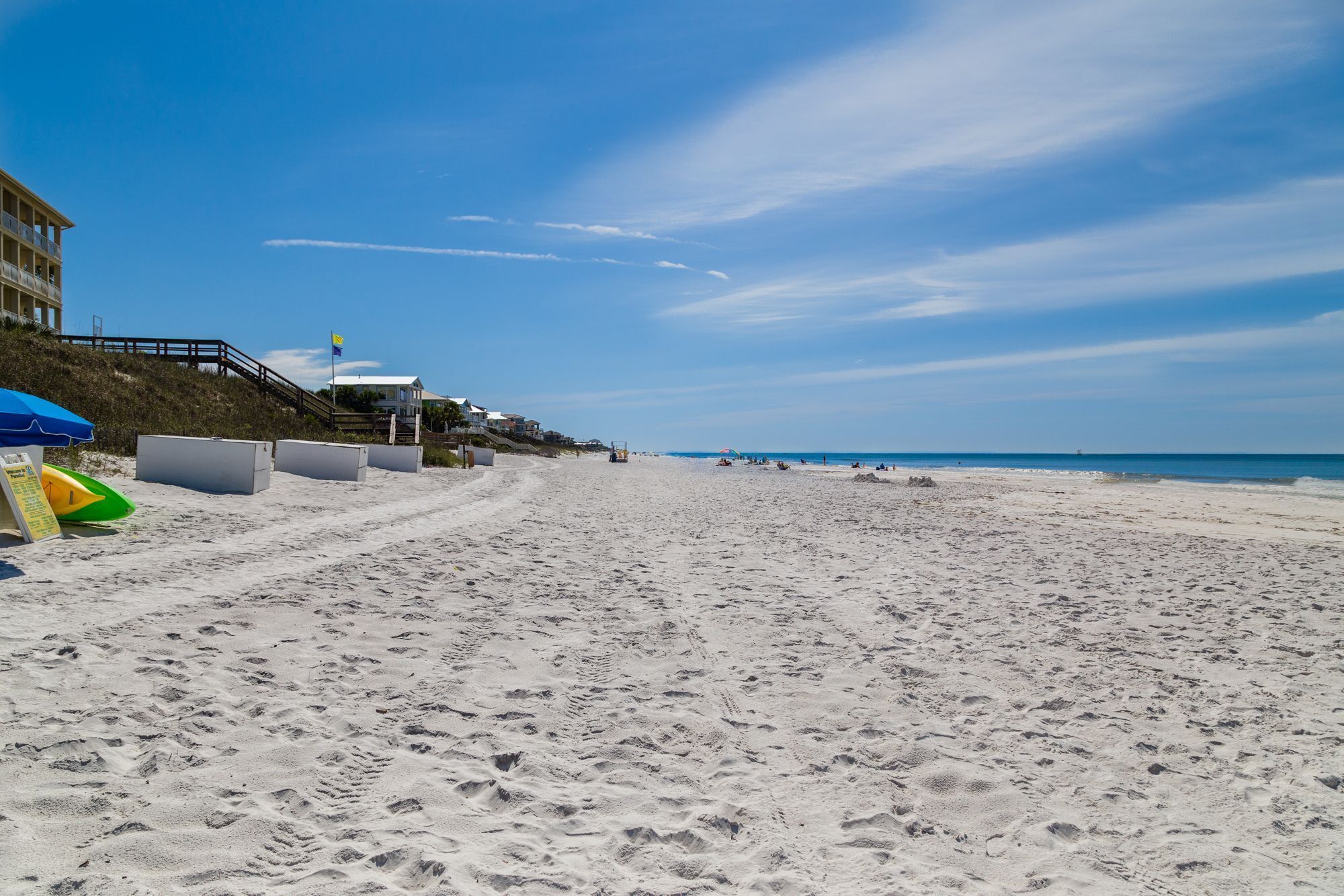 A beach with a sandy shore, a wooden walkway, and a building with a flag.