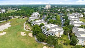 Vista aérea de un campo de golf con una zona residencial, que incluye edificios de varios pisos y una torre destacada.