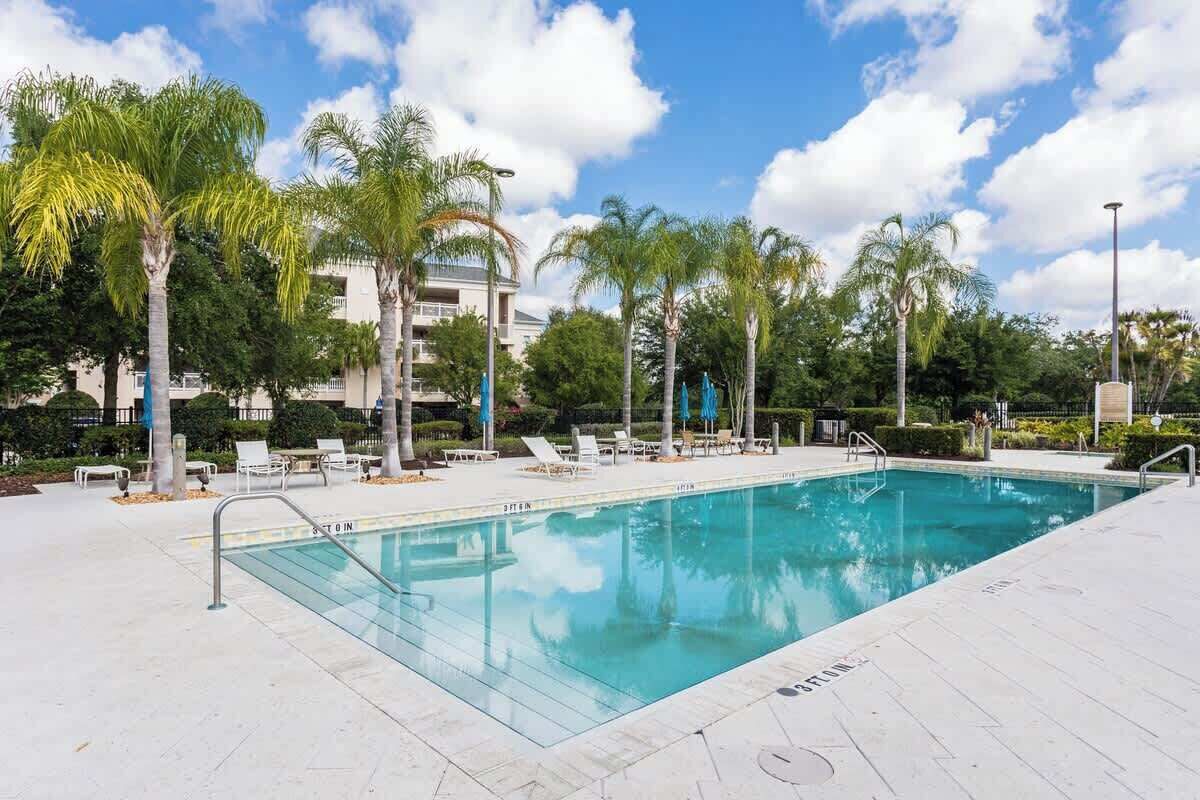 A swimming pool with lounge chairs and palm trees, surrounded by a building.