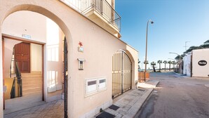 A building with a large archway entrance, a balcony, and a street view with palm trees. - I Tre Golfi Beach Apartments (San Vito Lo Capo)