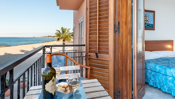 A balcony with a view of the beach, a bottle of wine, and snacks on a table. - I Tre Golfi Beach Apartments (San Vito Lo Capo)
