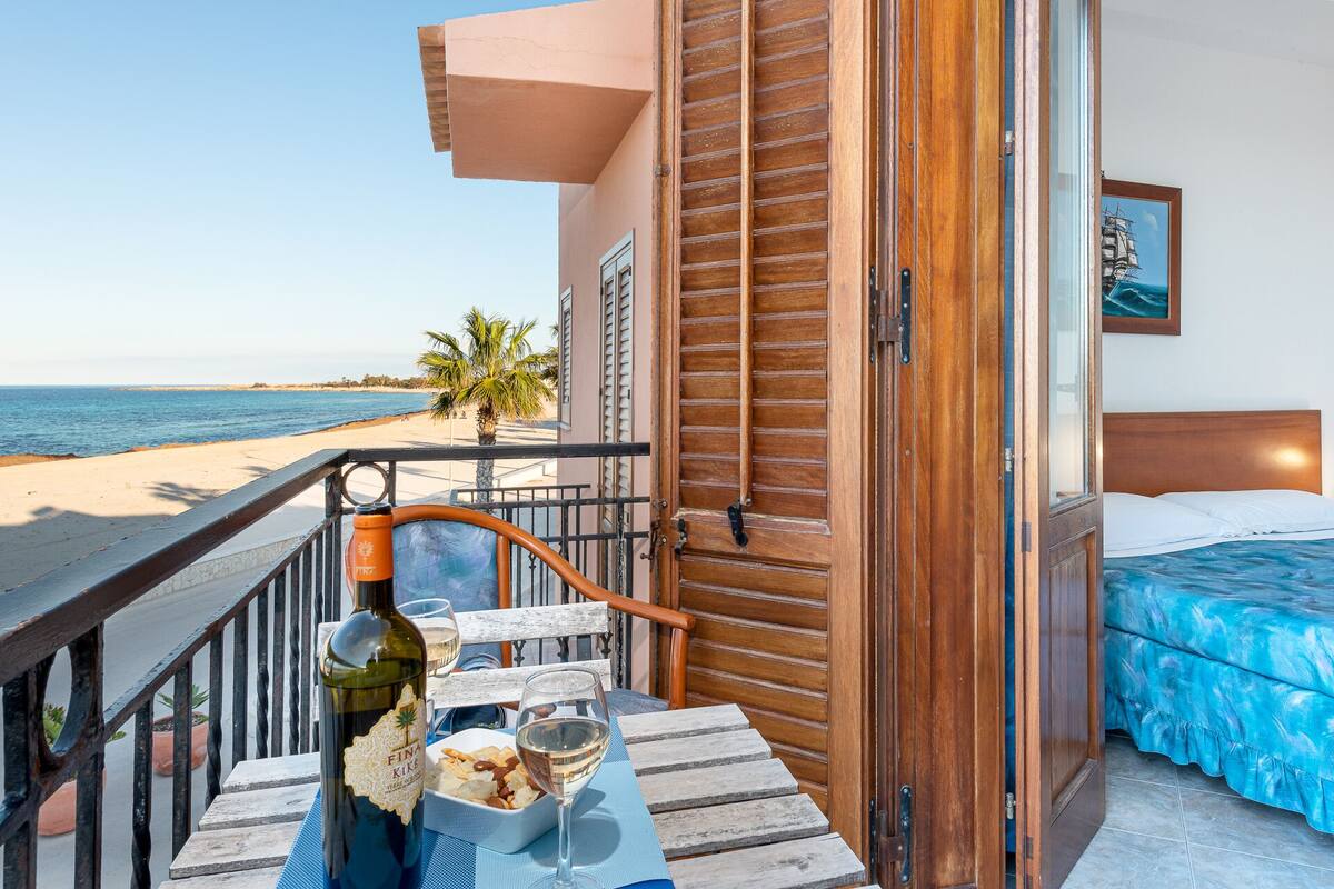 Een balkon met uitzicht op het strand, een fles wijn en lekkernijen op een tafel.