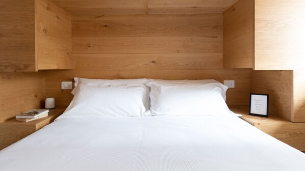A bed with white linens in a wooden room with built-in nightstands.