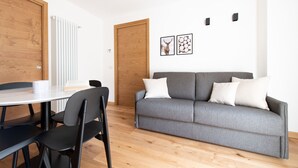 A modern living room with a grey sofa, two black chairs, a white table, and a wooden door. - Al Forte 6 - One Bedroom Apartment, Sleeps 3 (Valdisotto)