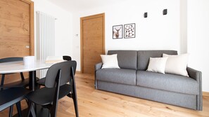 A modern living room with a grey sofa, black chairs, a round table, and a wooden door.