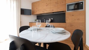 A modern kitchen with wooden cabinets, a built-in microwave, and a dining table set with clear glasses and plates.