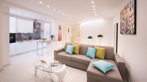 Een moderne woonkamer met een bank, een glazen salontafel en een keuken op de achtergrond.