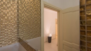 Een gang met een betegelde muur, een plant in pot en een deur naar een andere kamer.