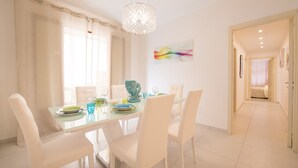 Een eetgedeelte met een glazen tafel, witte stoelen en een kroonluchter.