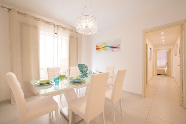 A dining area with a glass table, white chairs, and a chandelier. - Stylish Apartment Close to beach - Al Corso 8 by AMALFIVACATION.IT (MINORI)