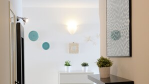 A hallway with a white door, a white cabinet, and a black shelf with plants. - Ananas - Sea View - Fruit Flats by AMALFIVACATION.IT (MINORI)
