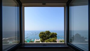 Vista desde una ventana con vista a una playa, barcos, un árbol y una zona de piscina.