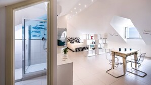 Un interior moderno con ducha de vidrio, zona de comedor con mesa y sillas de madera, y sala de estar con sofá y mesa de centro.