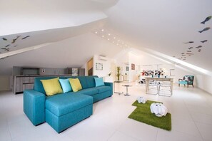 Relax in this spacious living area with a sofa, dining table, and kitchen in the background.