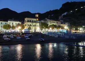Zona costera con barcos, una torre del reloj y edificios iluminados.