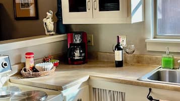A kitchen with a stove, coffee maker, wine bottle, and a sink.