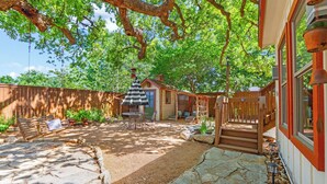 A backyard with a stone patio, a wooden bench, a swing, a small table with chairs, and a building with a red trim and windows. - Cozy & Convenient, 1/2 block off Main St. in Boerne, WALK EVERYWHERE! (Boerne)
