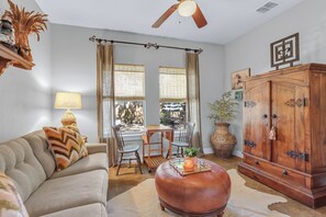 Una sala de estar con sofá, reposapiés, aparador de madera, mesa de comedor con sillas y ventilador de techo.