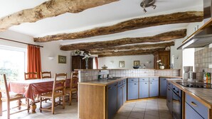 A kitchen with exposed wooden beams, a dining area with a table and chairs, and a kitchen island with cabinets. - Appartement "kerouac", Maison du 18ème Avec Wifi, Proche des Plages de Sable fin (Carnac)