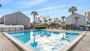 Ein rechteckiger Pool mit zwei Bereichen, umgeben von Liegestühlen und Palmen.