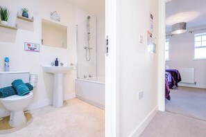 Une salle de bain moderne équipée de toilettes, d’un lavabo et d’une douche. Il y a des serviettes sur le sol et un panneau accroché au mur.
