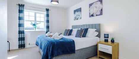 A bedroom with a bed, a bedside table, a window with curtains, and wall art.