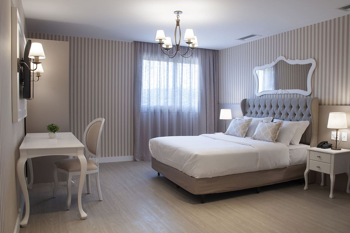 A neatly arranged bedroom with a bed, bedside tables, a desk, and a chair.