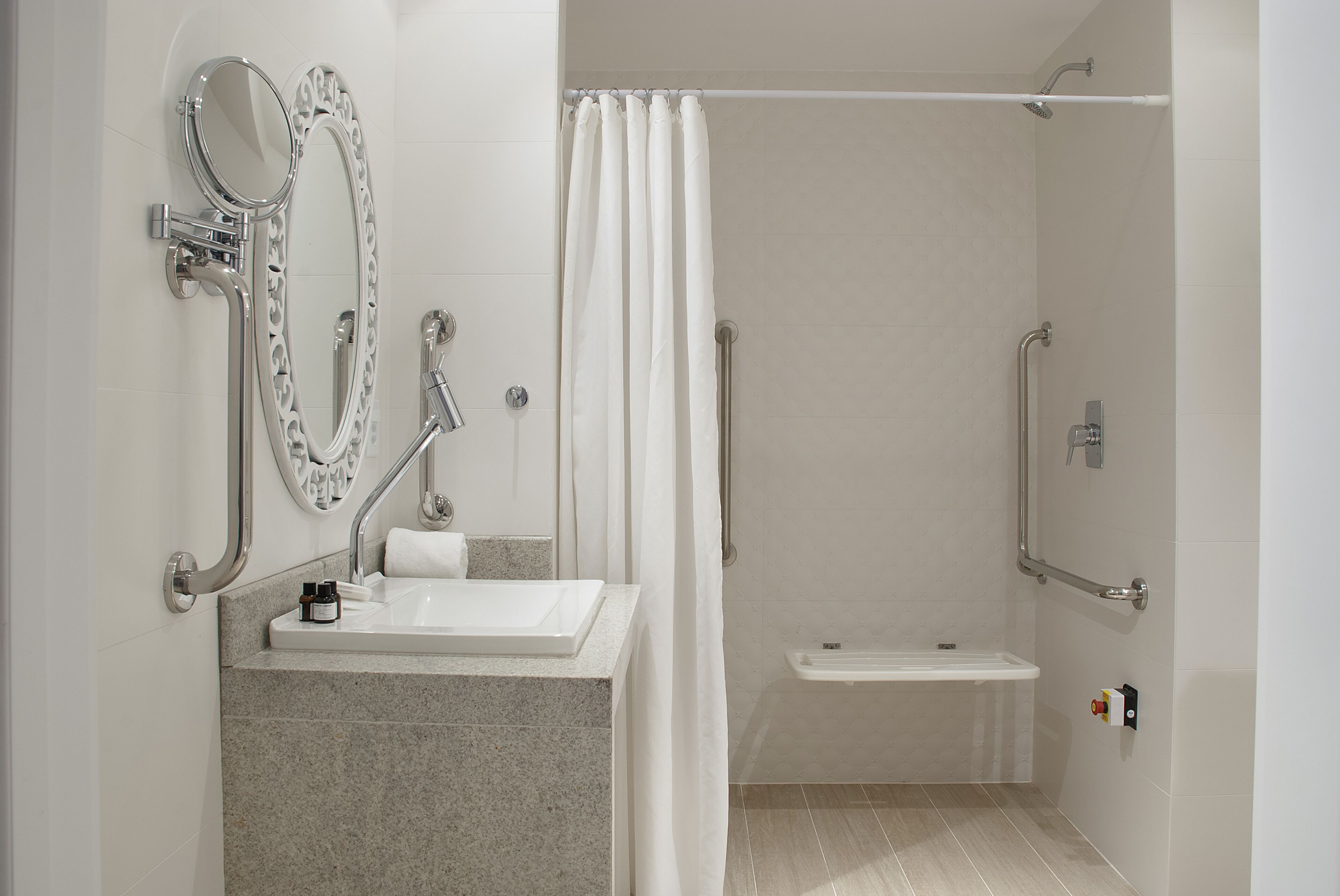 A modern bathroom with a vanity, mirror, shower, and grab bars.