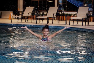 Una piscina con una persona a nuoto, circondata da sdraio e un’area coperta con tavoli e sedie.