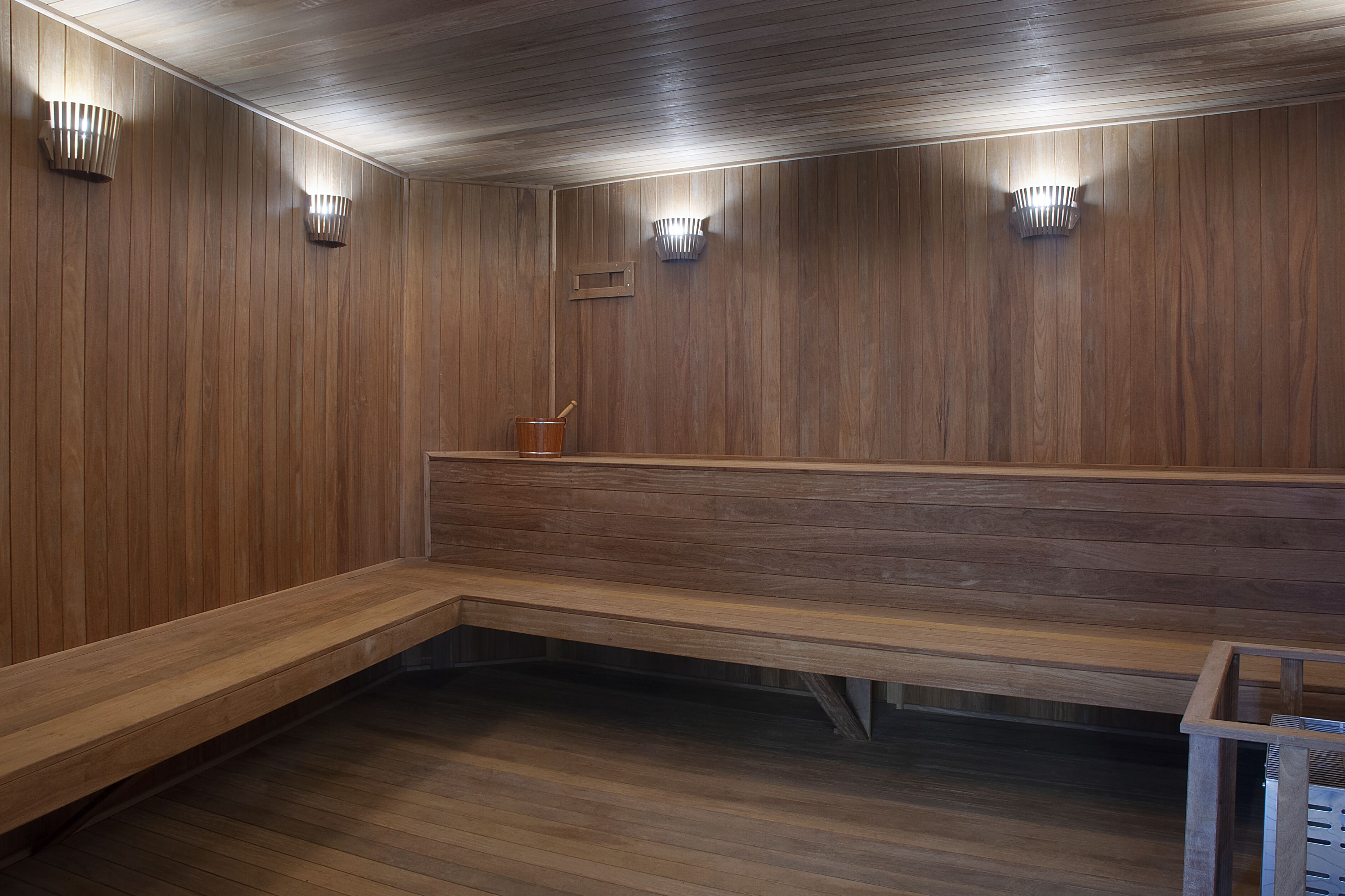 A wooden bench in a room with wooden walls and ceiling, and three wall-mounted light fixtures.