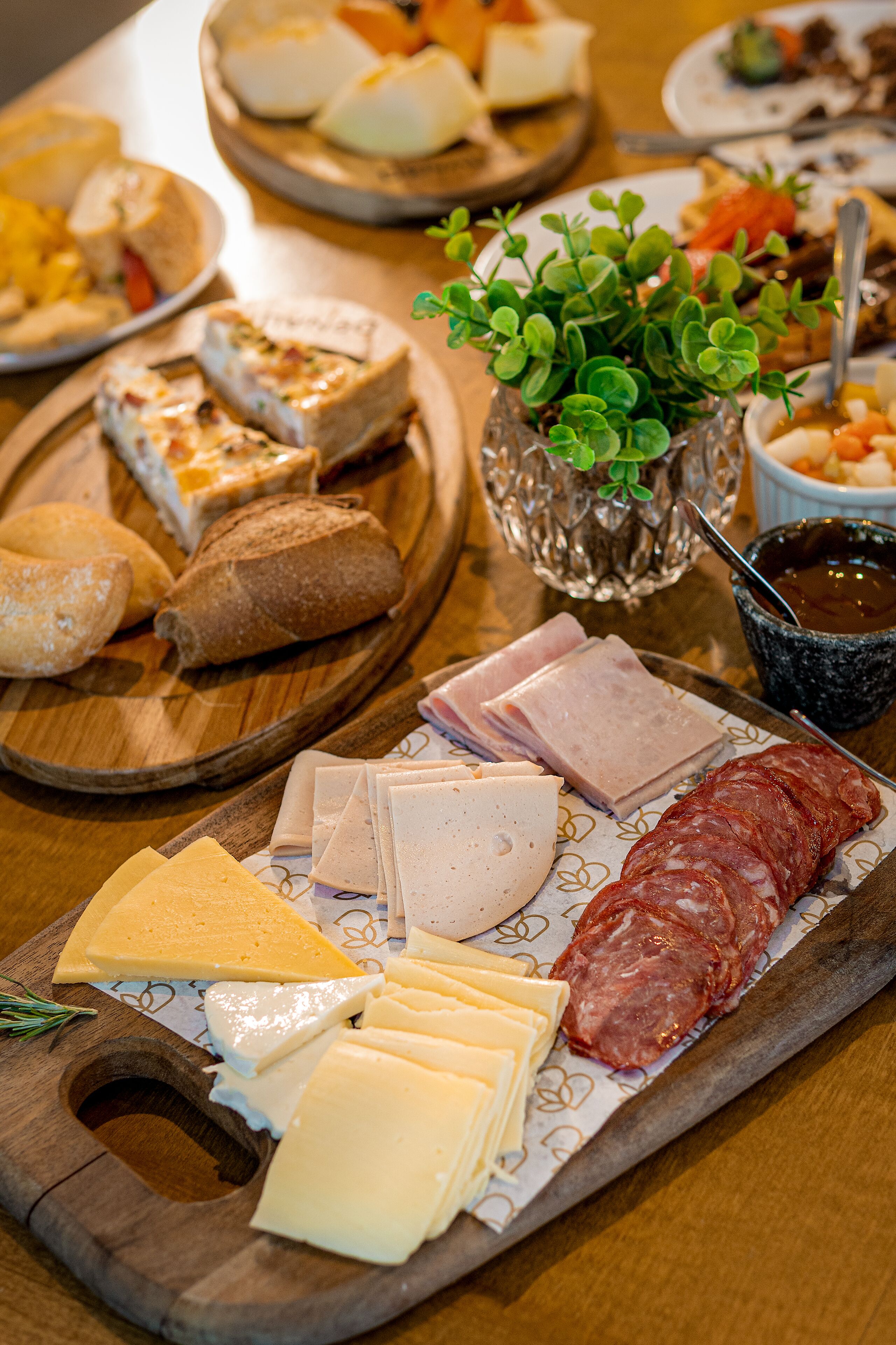 A wooden board with various cheeses, meats, and bread.