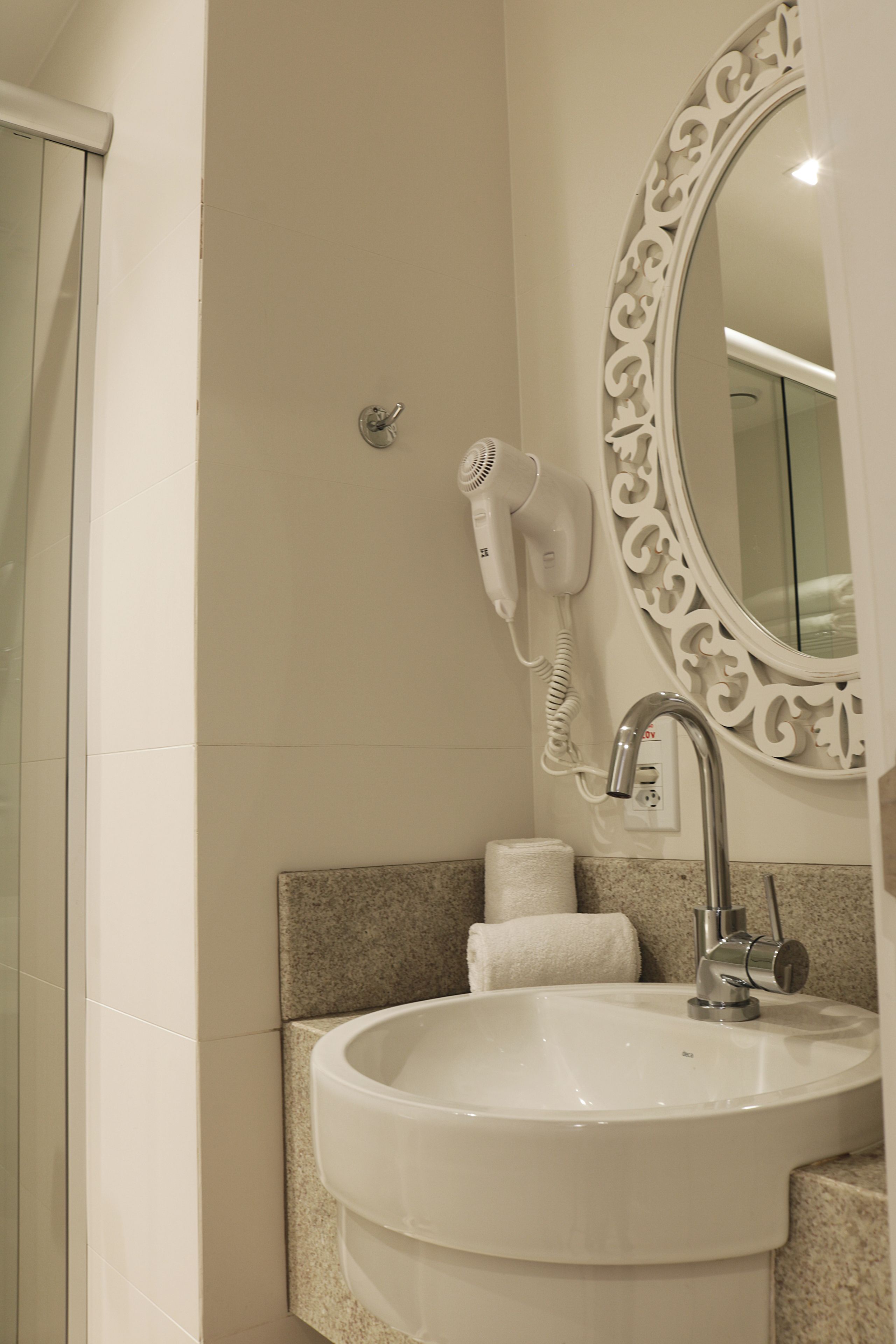 A bathroom with a sink, a mirror, a hairdryer, and a towel.