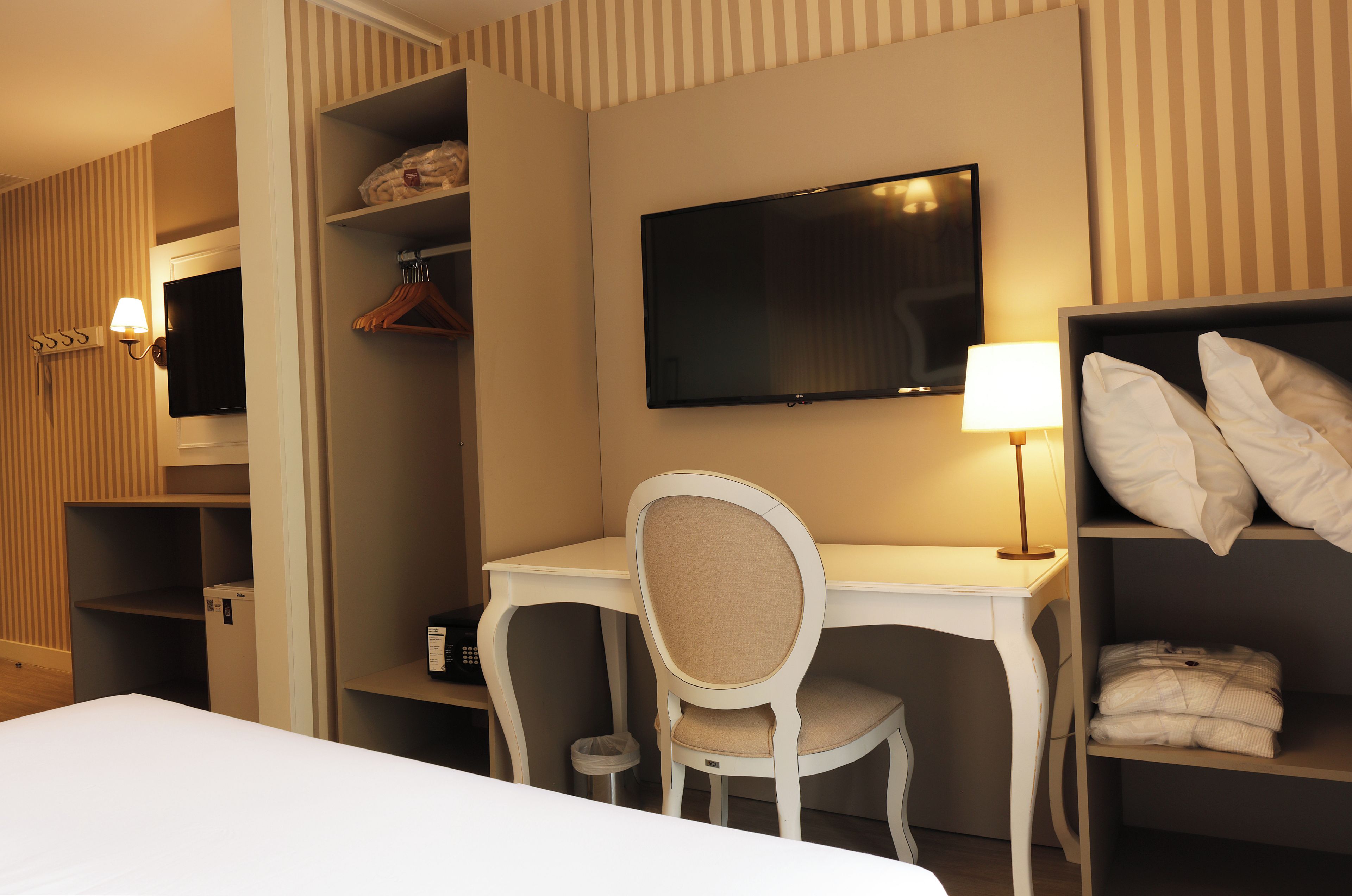 A hotel room with a bed, a desk, a chair, a TV, a lamp, and a wardrobe.