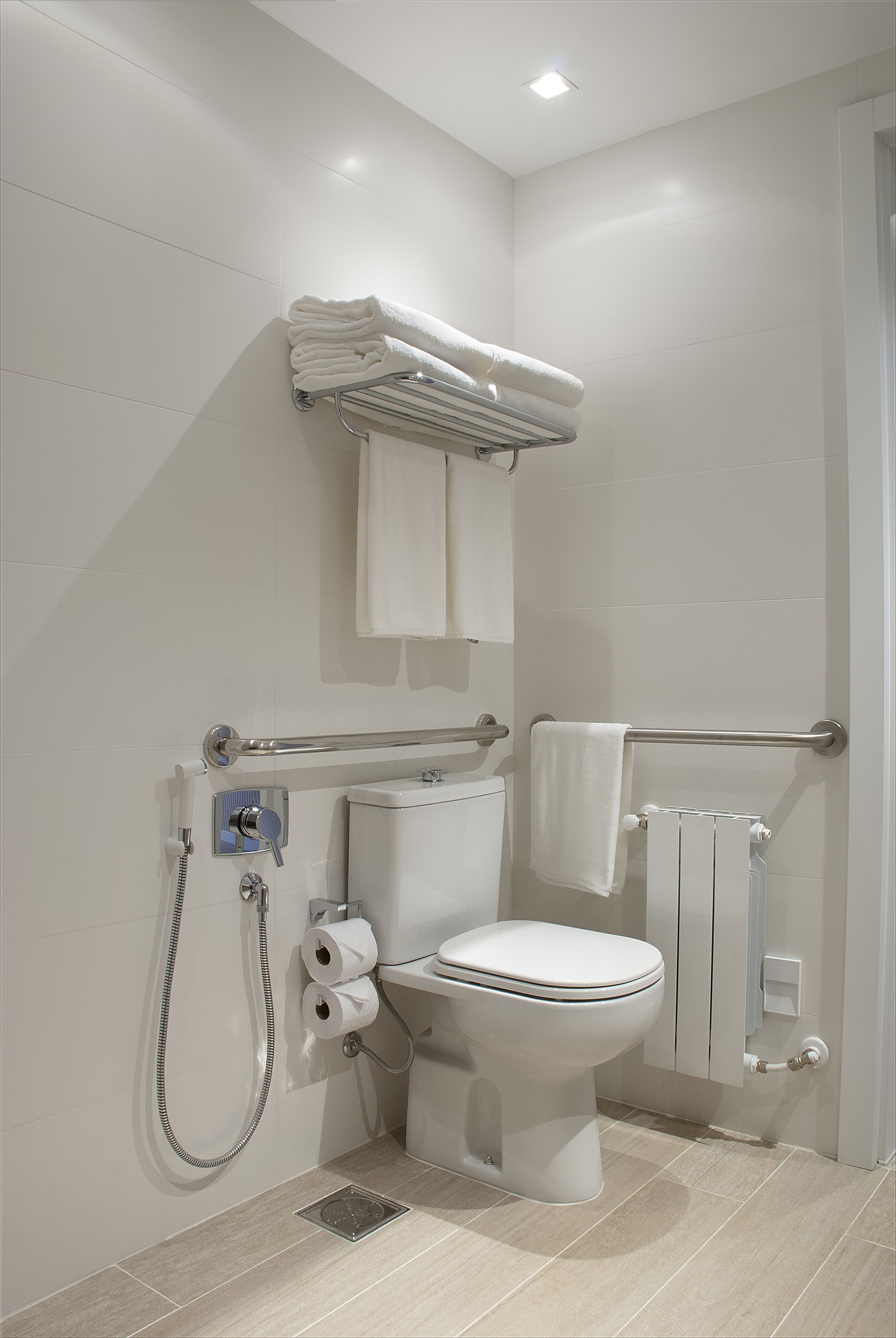 Een moderne badkamer met toilet, bidet en een handdoekhouder.