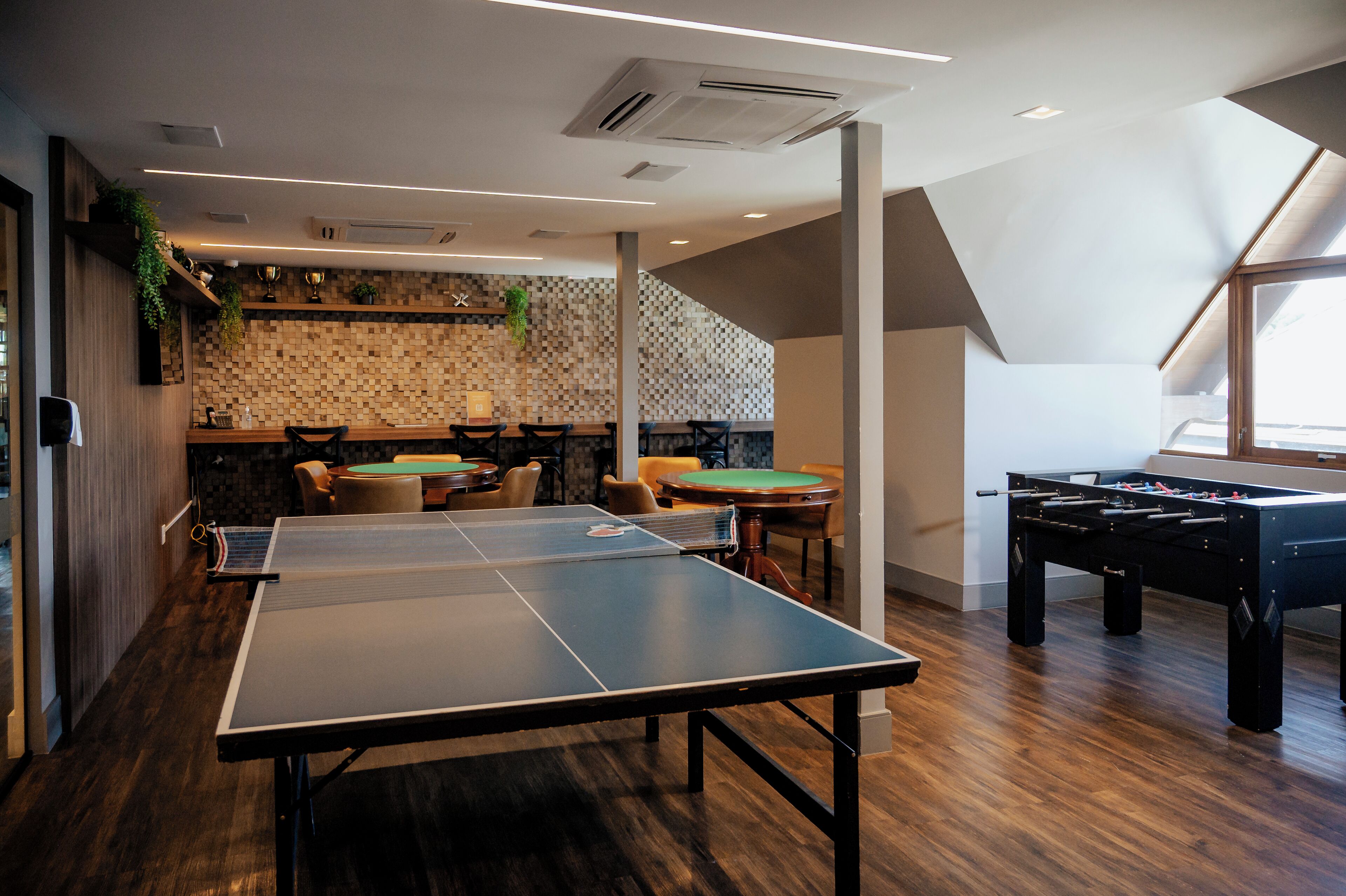 Una habitación con mesa de ping pong, mesa de fútbol de mesa y zona de bar con taburetes y una mesa verde.